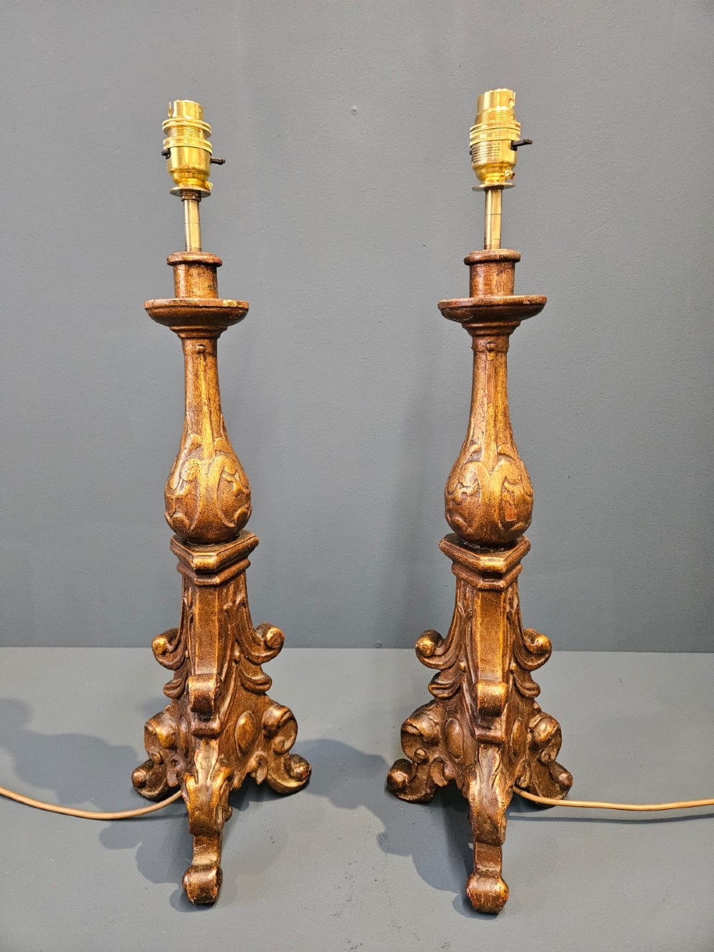 A pair of tall carved timber candlestick table lamps with aged gold gilding and scrolled bases.
