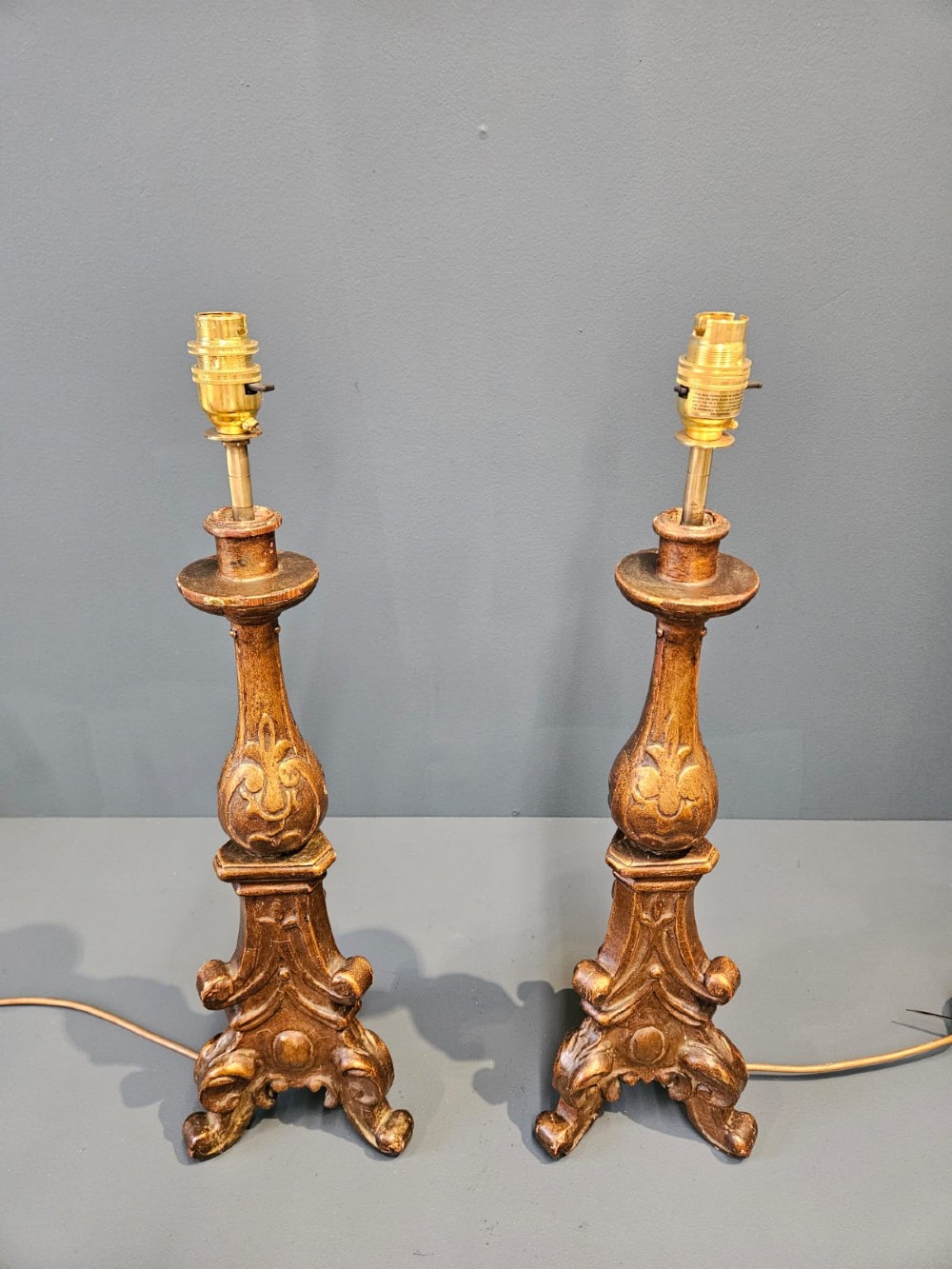 A pair of tall carved timber candlestick table lamps with aged gold gilding and scrolled bases. View V