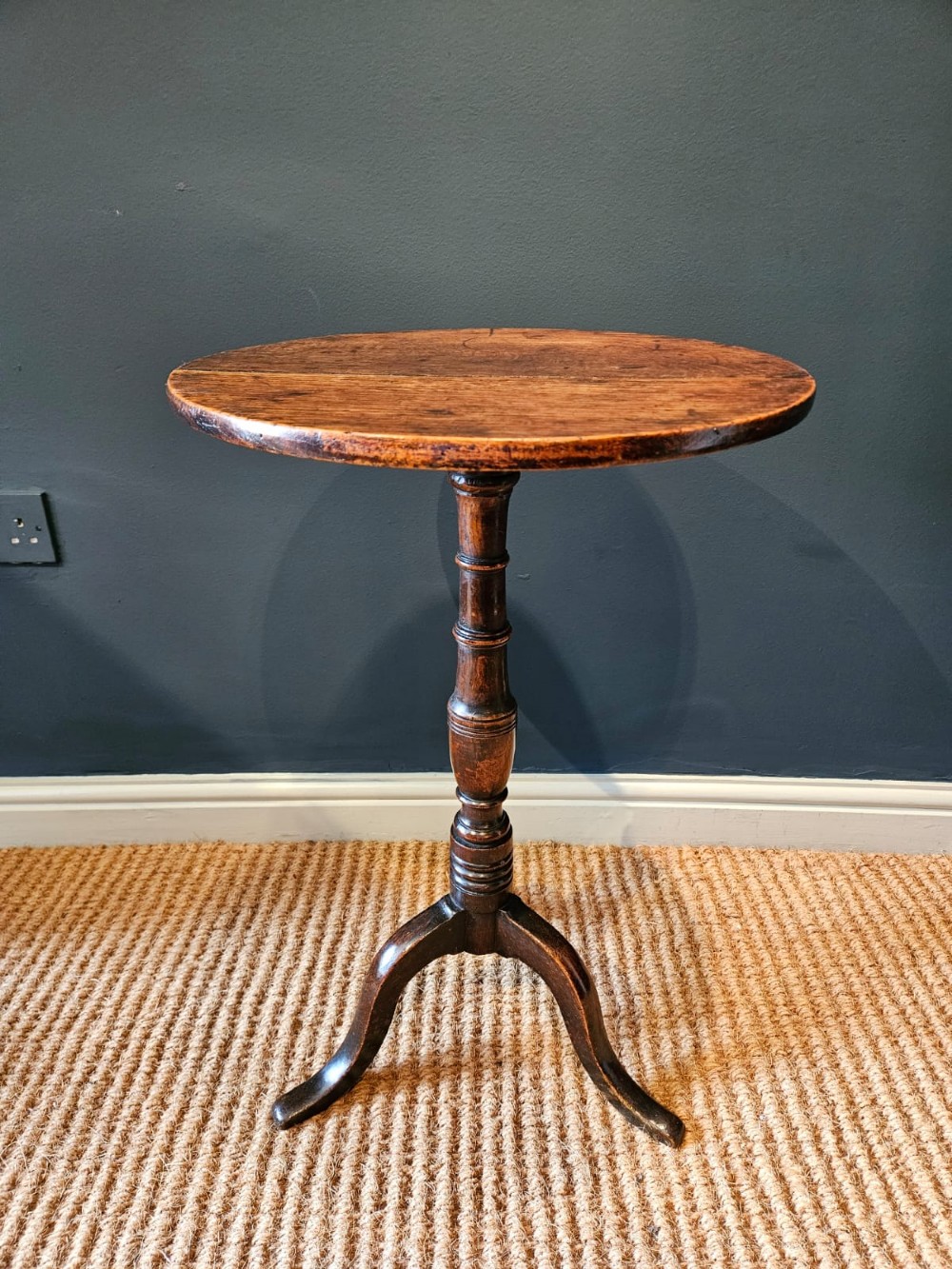 A small George III period oak tripod table featuring a circular top supported by a turned central column and three curved legs.