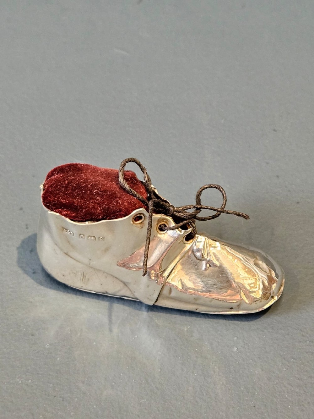 An Edwardian sterling silver pin cushion crafted in the form of a childs boot with a dark red velvet cushion top and cord laces.