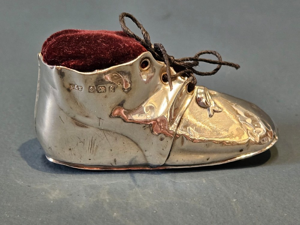 An Edwardian sterling silver pin cushion crafted in the form of a childs boot with a dark red velvet cushion top and cord laces. View II