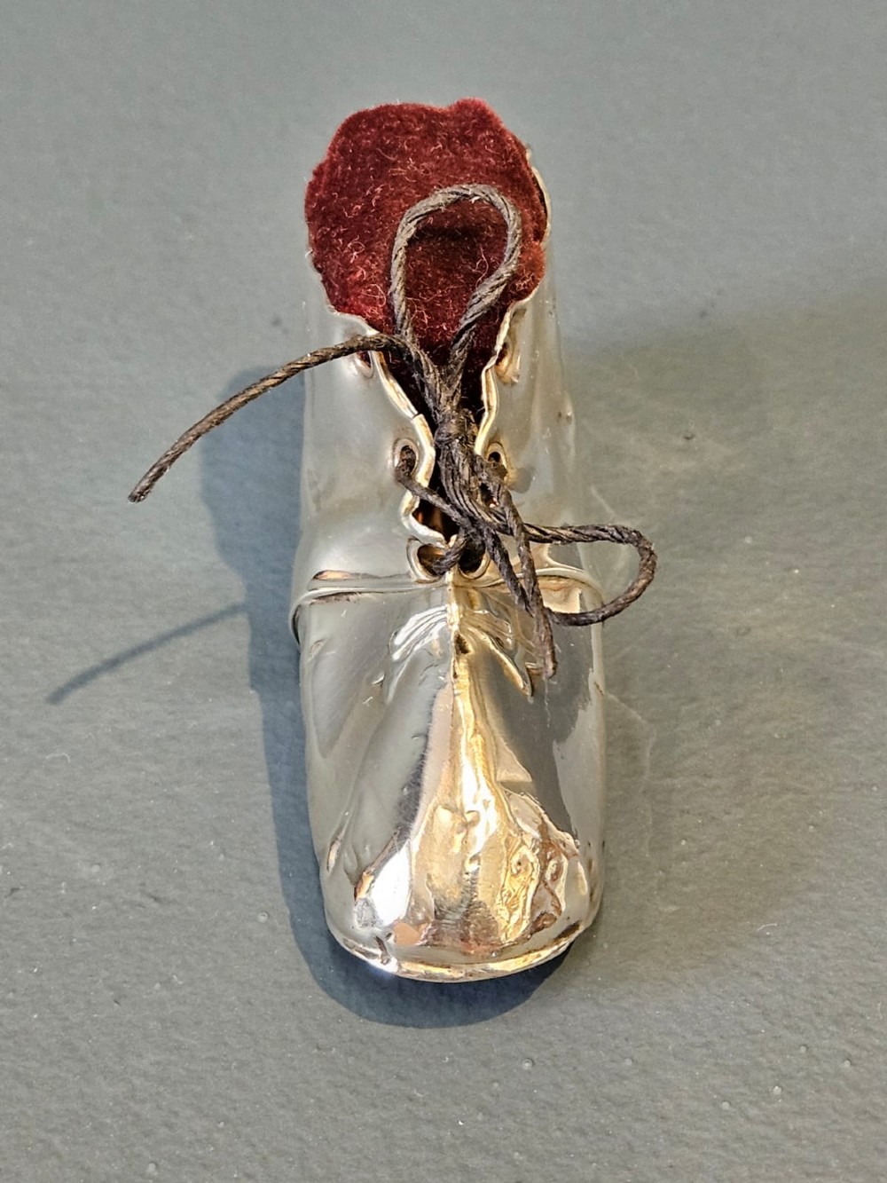 An Edwardian sterling silver pin cushion crafted in the form of a childs boot with a dark red velvet cushion top and cord laces. View V