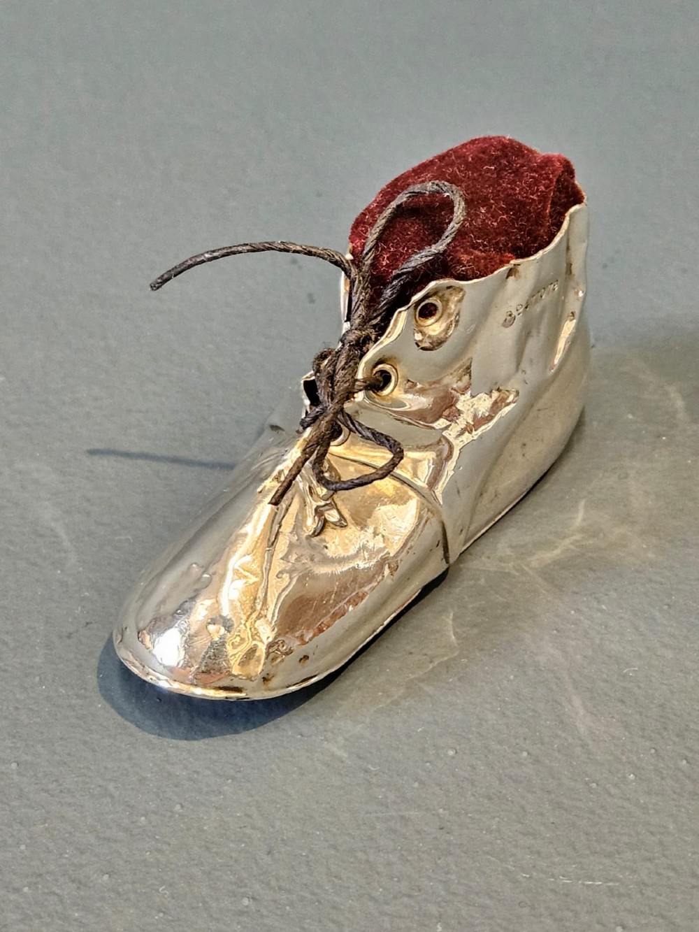 An Edwardian sterling silver pin cushion crafted in the form of a childs boot with a dark red velvet cushion top and cord laces. View VII