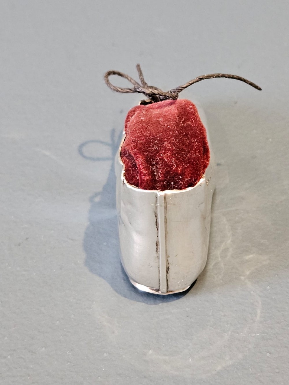 An Edwardian sterling silver pin cushion crafted in the form of a childs boot with a dark red velvet cushion top and cord laces. View VIII