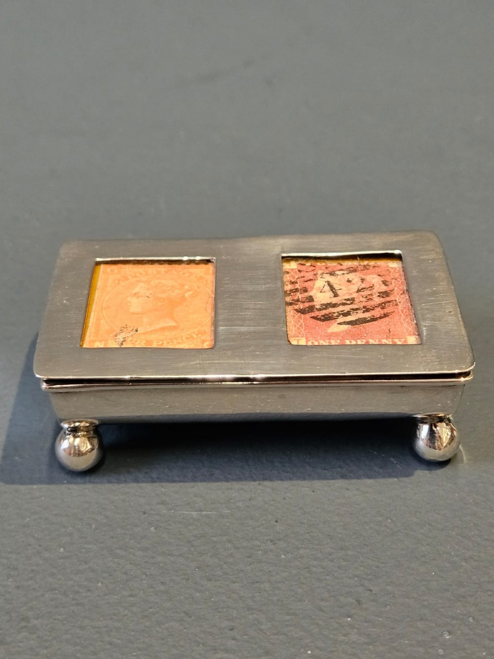 A small rectangular Victorian silver stamp box raised on four ball feet with two glass apertures on the lid displaying postage stamps. View III