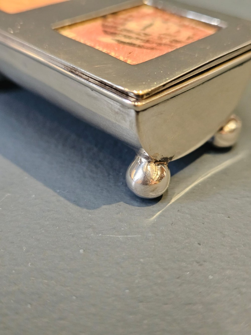 A small rectangular Victorian silver stamp box raised on four ball feet with two glass apertures on the lid displaying postage stamps. View VI