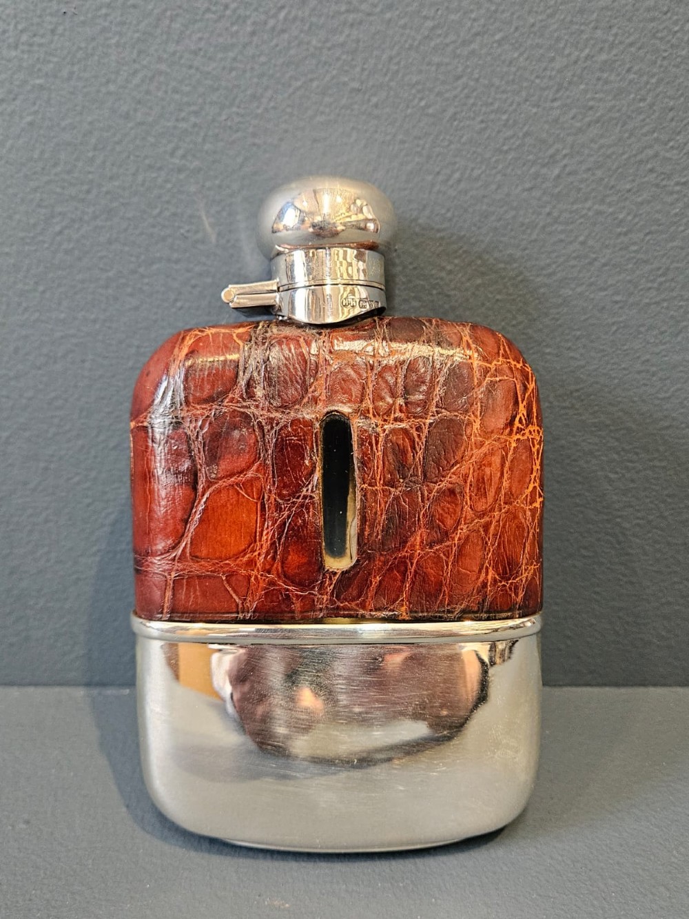 An antique silver hip flask partially encased in brown textured crocodile skin with a bayonet cap and removable base cup.