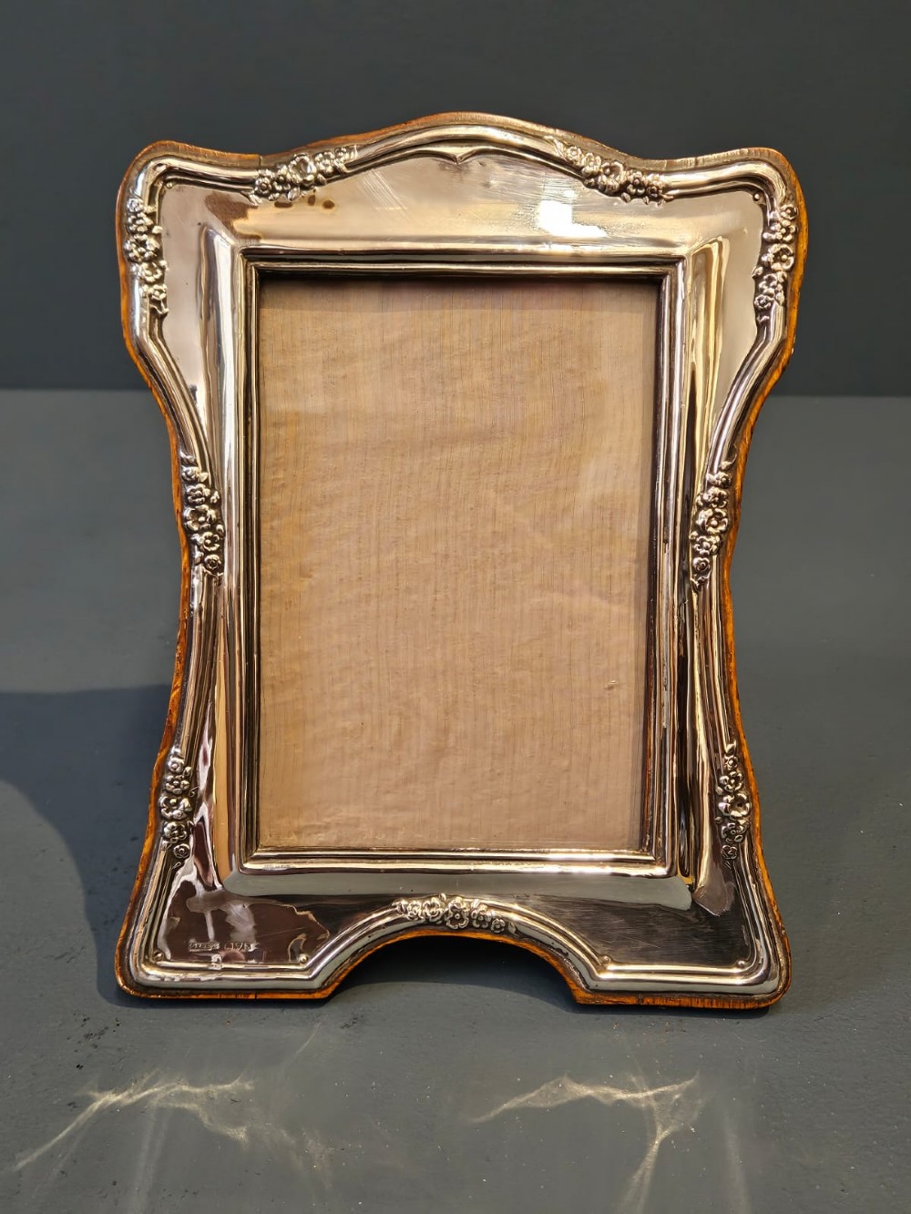 An Edwardian silver photo frame featuring embossed floral motifs along the shaped edges and a wooden backing.