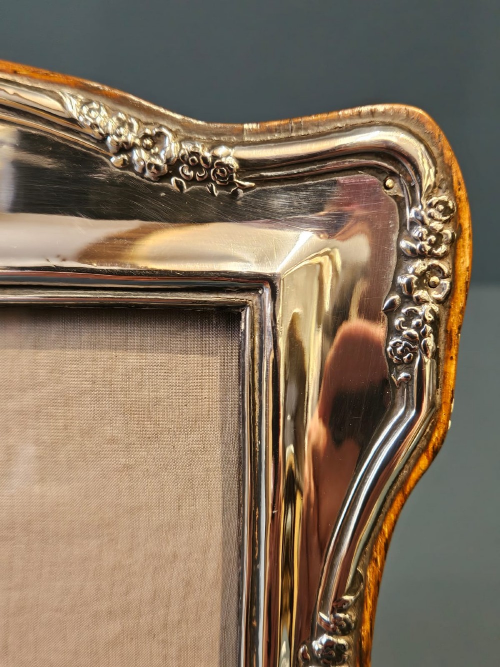 An Edwardian silver photo frame featuring embossed floral motifs along the shaped edges and a wooden backing. View II