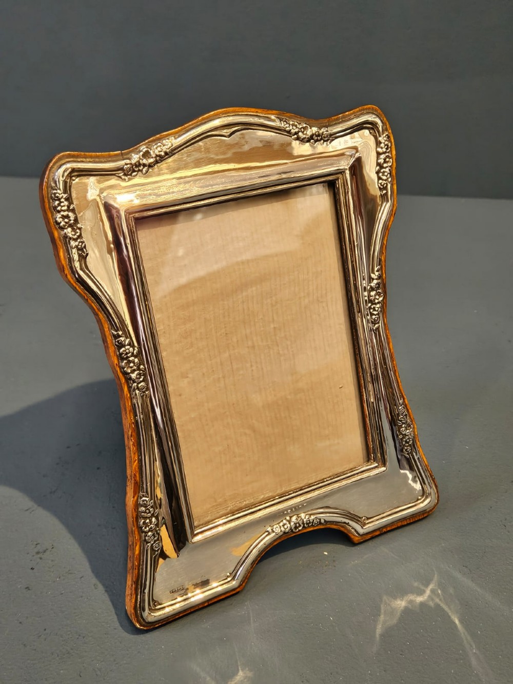 An Edwardian silver photo frame featuring embossed floral motifs along the shaped edges and a wooden backing. View III
