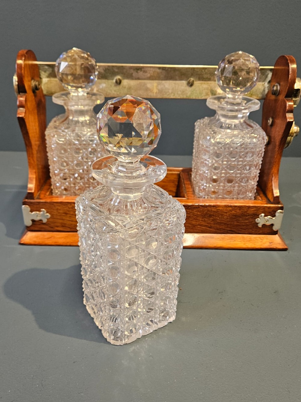 A Victorian oak three-bottle tantalus featuring a wooden frame with silver-plated mounts and three cut-glass square decanters with round faceted stoppers. View III
