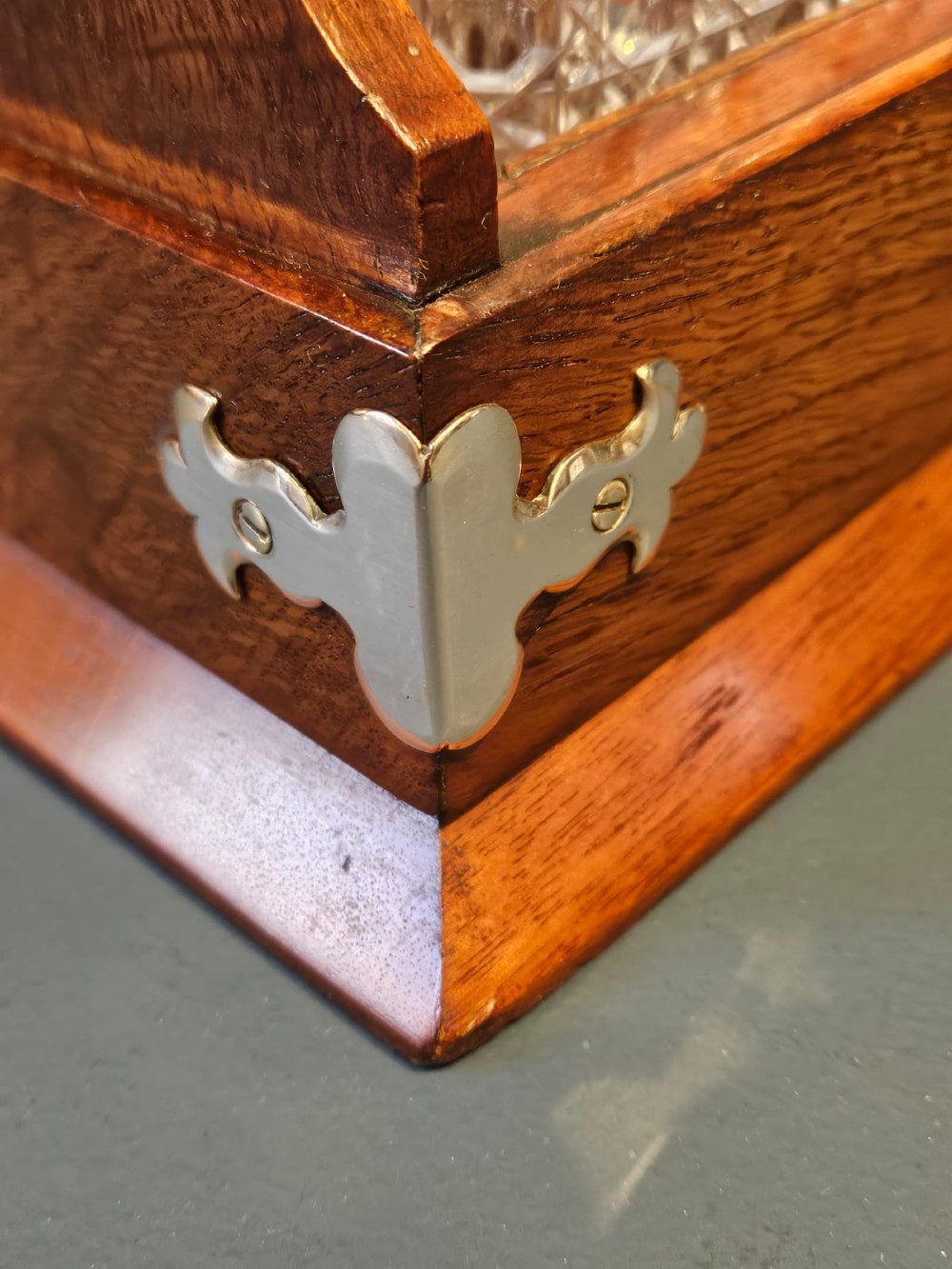 A Victorian oak three-bottle tantalus featuring a wooden frame with silver-plated mounts and three cut-glass square decanters with round faceted stoppers. View VI