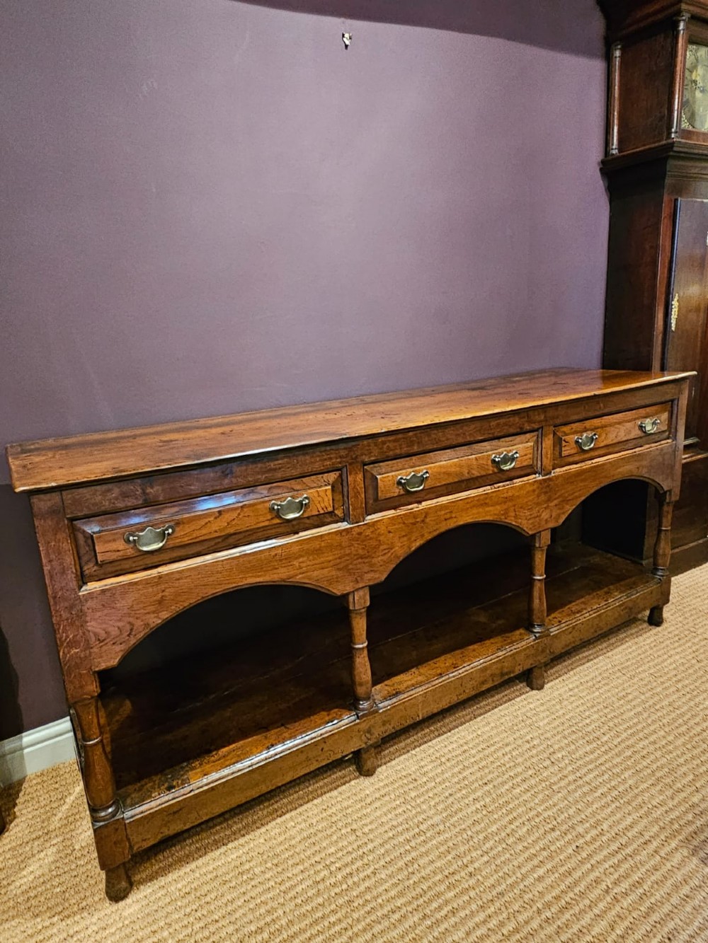 A George III oak open pot board dresser base featuring three drawers with brass drop handles, a shaped arched apron, and turned legs. View III