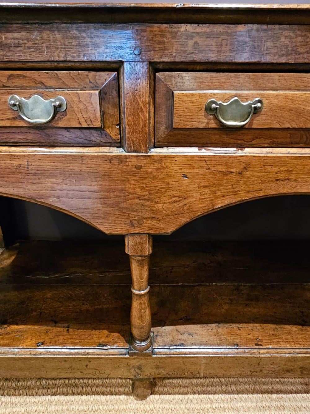 A George III oak open pot board dresser base featuring three drawers with brass drop handles, a shaped arched apron, and turned legs. View VI