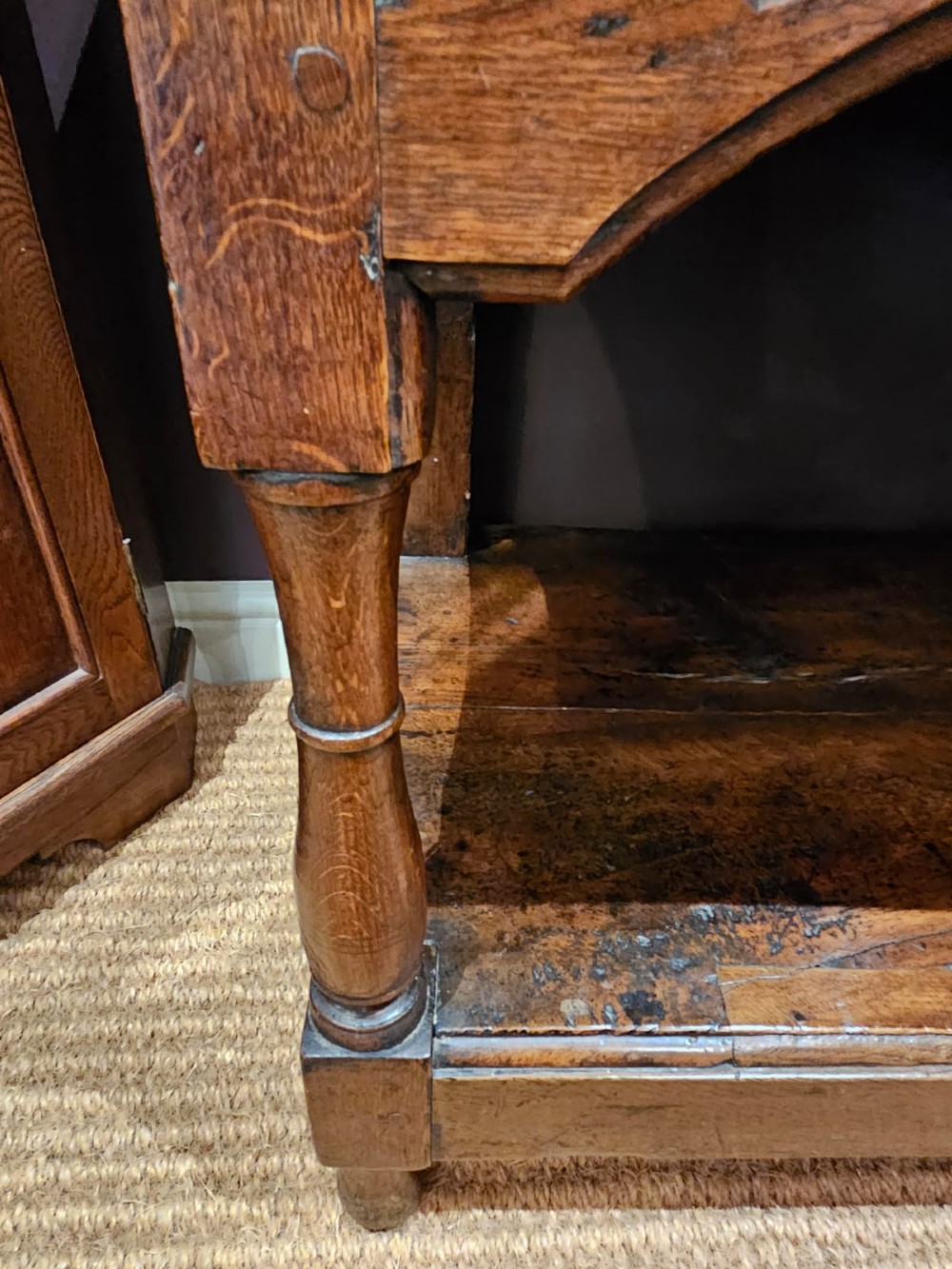 A George III oak open pot board dresser base featuring three drawers with brass drop handles, a shaped arched apron, and turned legs. View IX