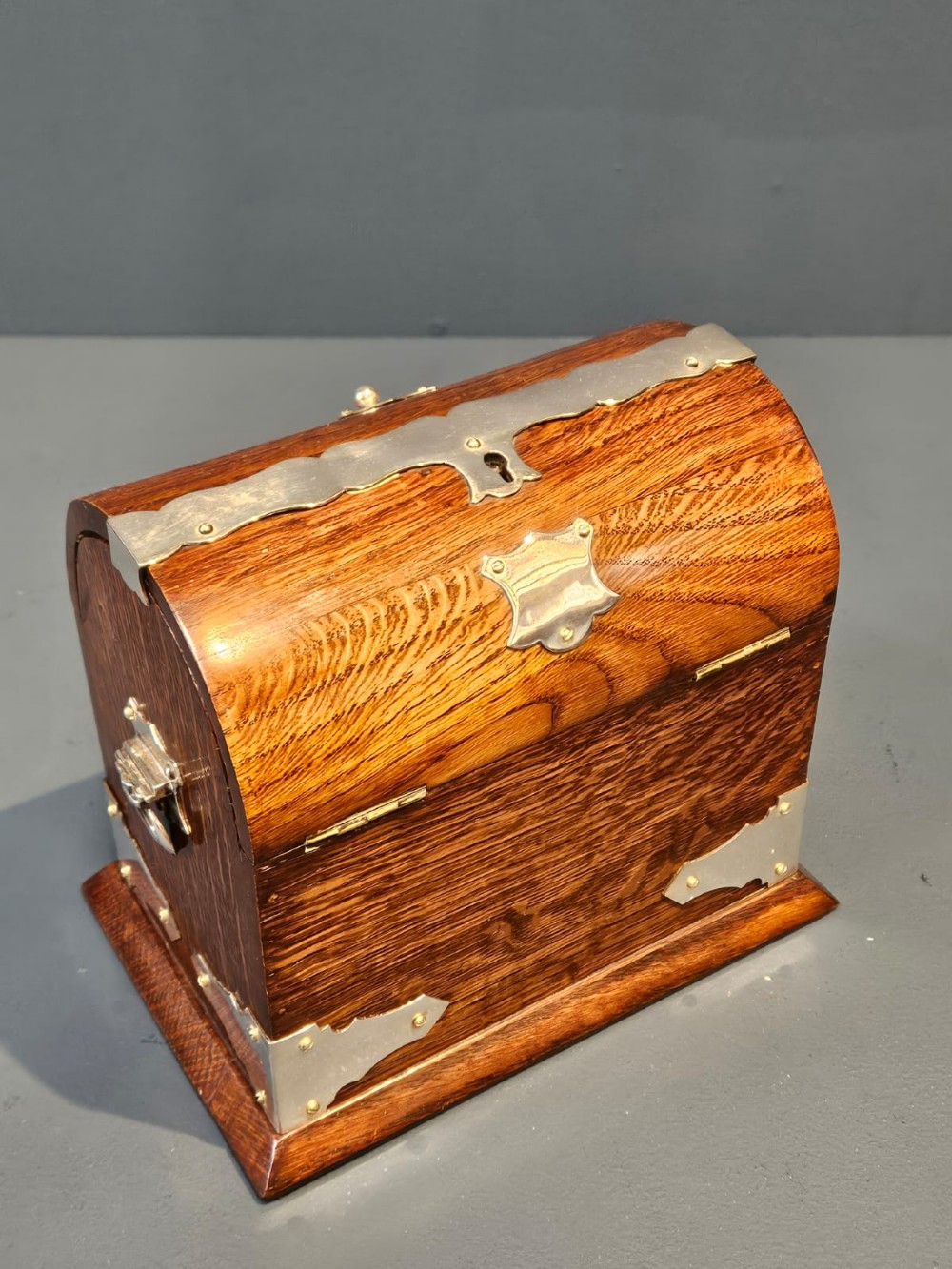A Victorian domed oak tea caddy featuring silver-plated corner mounts, an escutcheon, and side carrying handles. View V