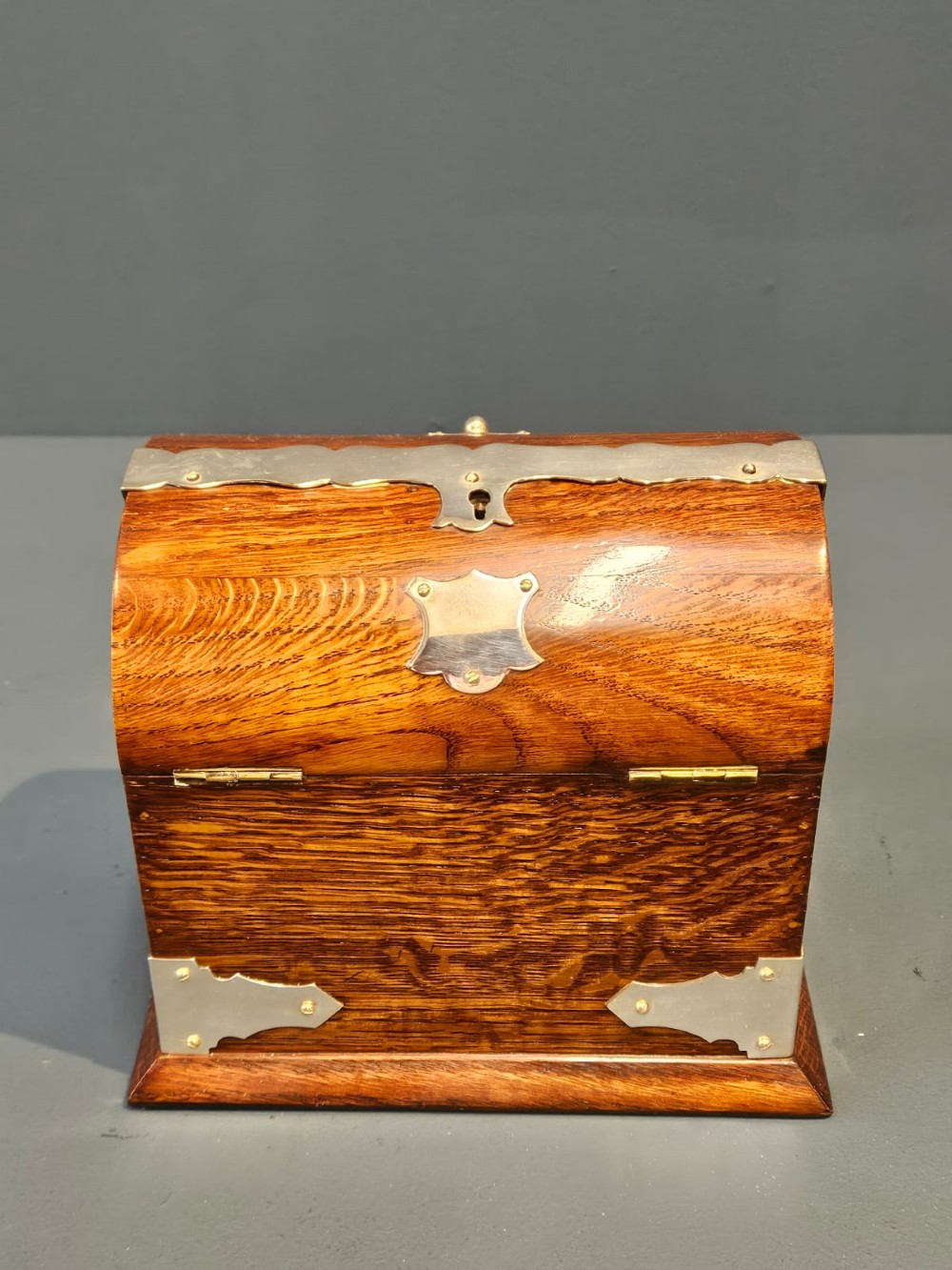 A Victorian domed oak tea caddy featuring silver-plated corner mounts, an escutcheon, and side carrying handles. View VII