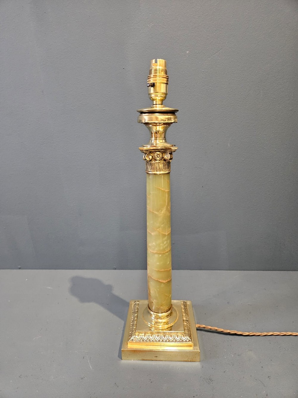A late Victorian table lamp featuring a brass Corinthian capital, a cylindrical green marble shaft, and a square stepped brass base.