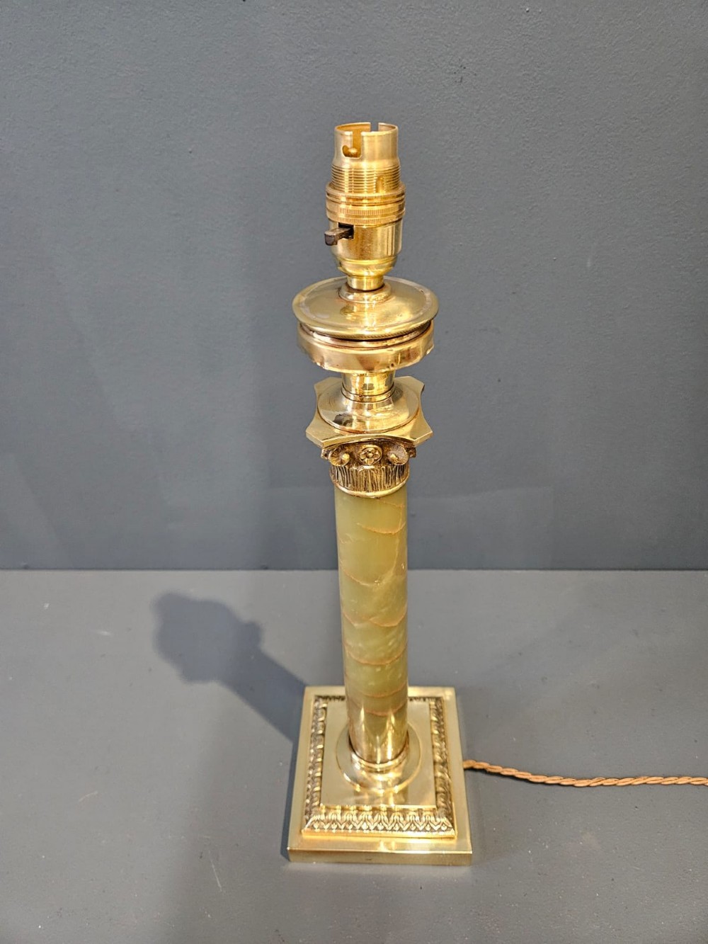 A late Victorian table lamp featuring a brass Corinthian capital, a cylindrical green marble shaft, and a square stepped brass base. View V