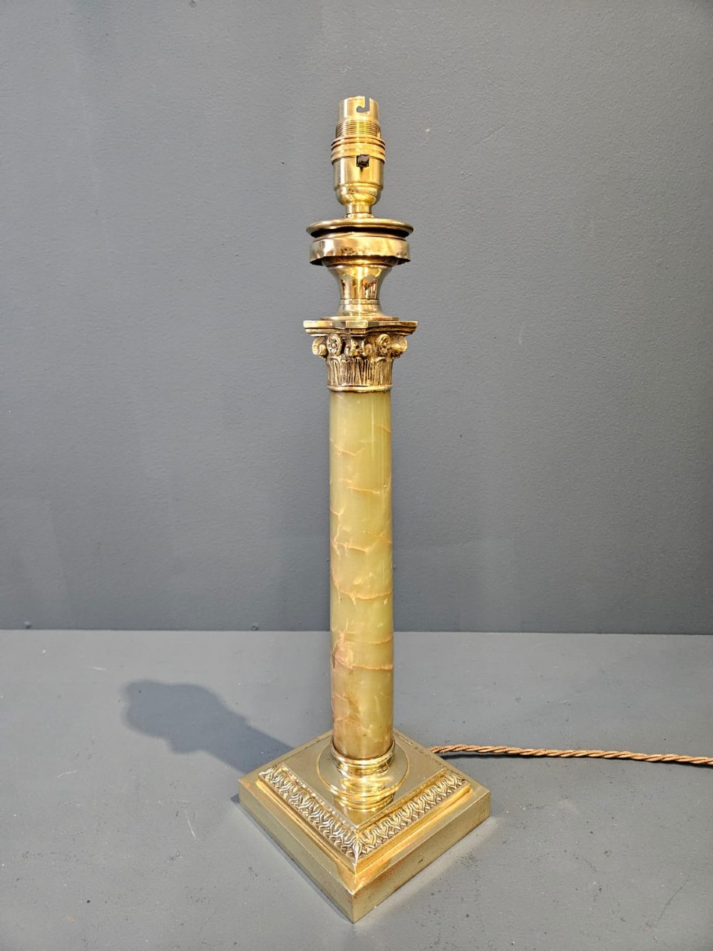 A late Victorian table lamp featuring a brass Corinthian capital, a cylindrical green marble shaft, and a square stepped brass base. View VI
