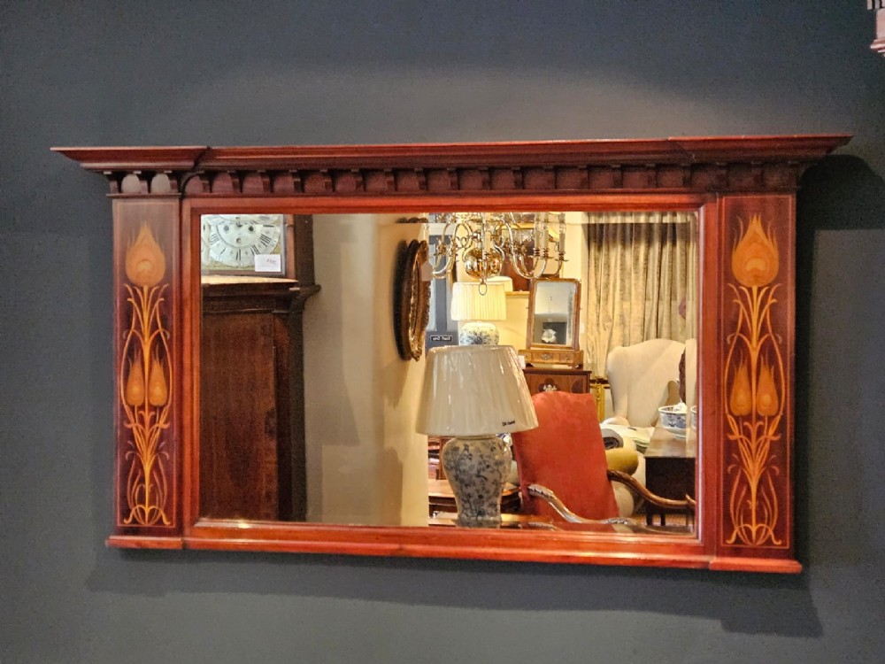 An Edwardian rectangular mahogany wall mirror featuring decorative marquetry side panels with stylised floral motifs and a corbelled top cornice.