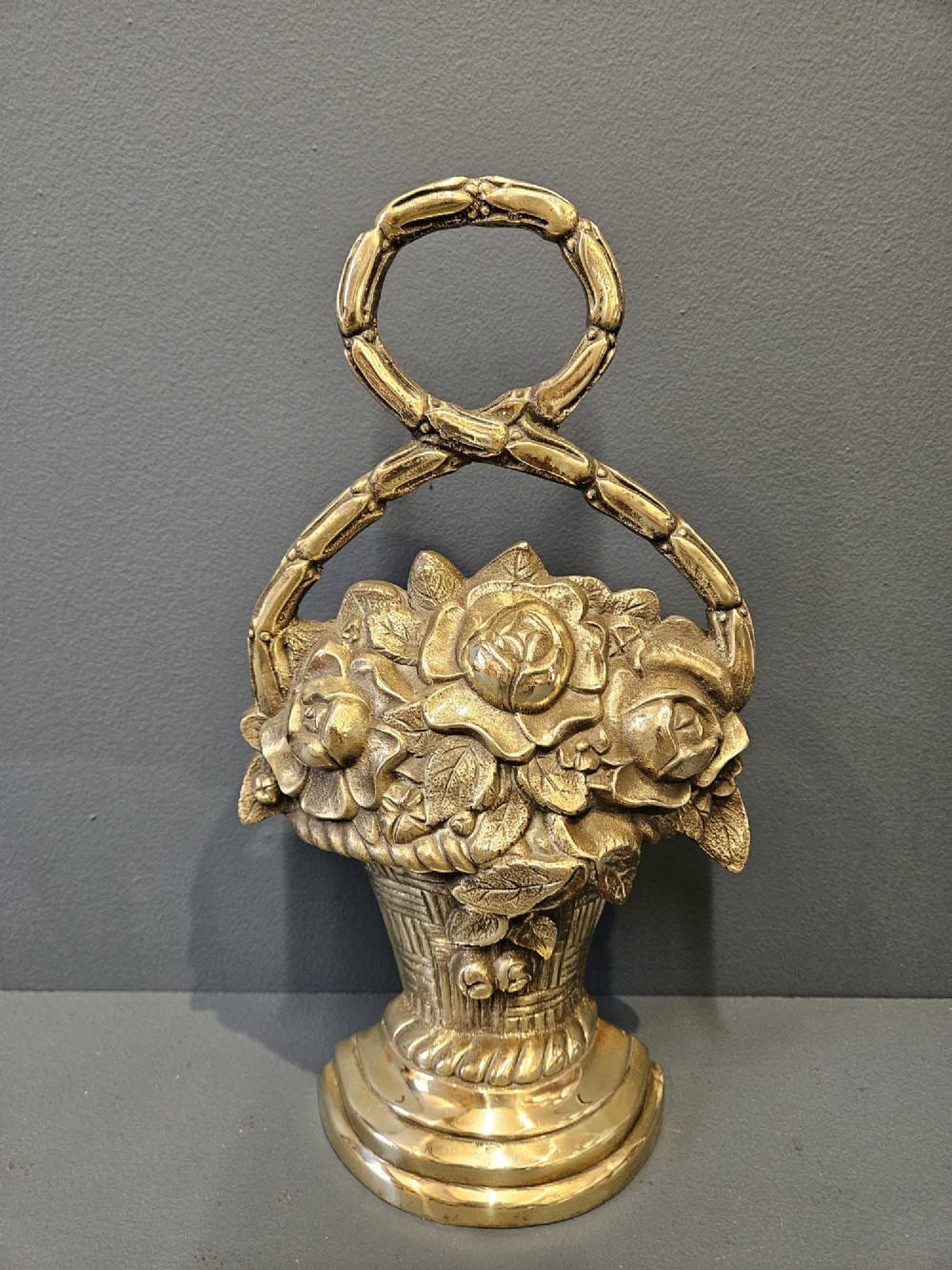 A Victorian cast brass doorstop featuring a detailed relief of roses inside a basket with an integrated loop handle.