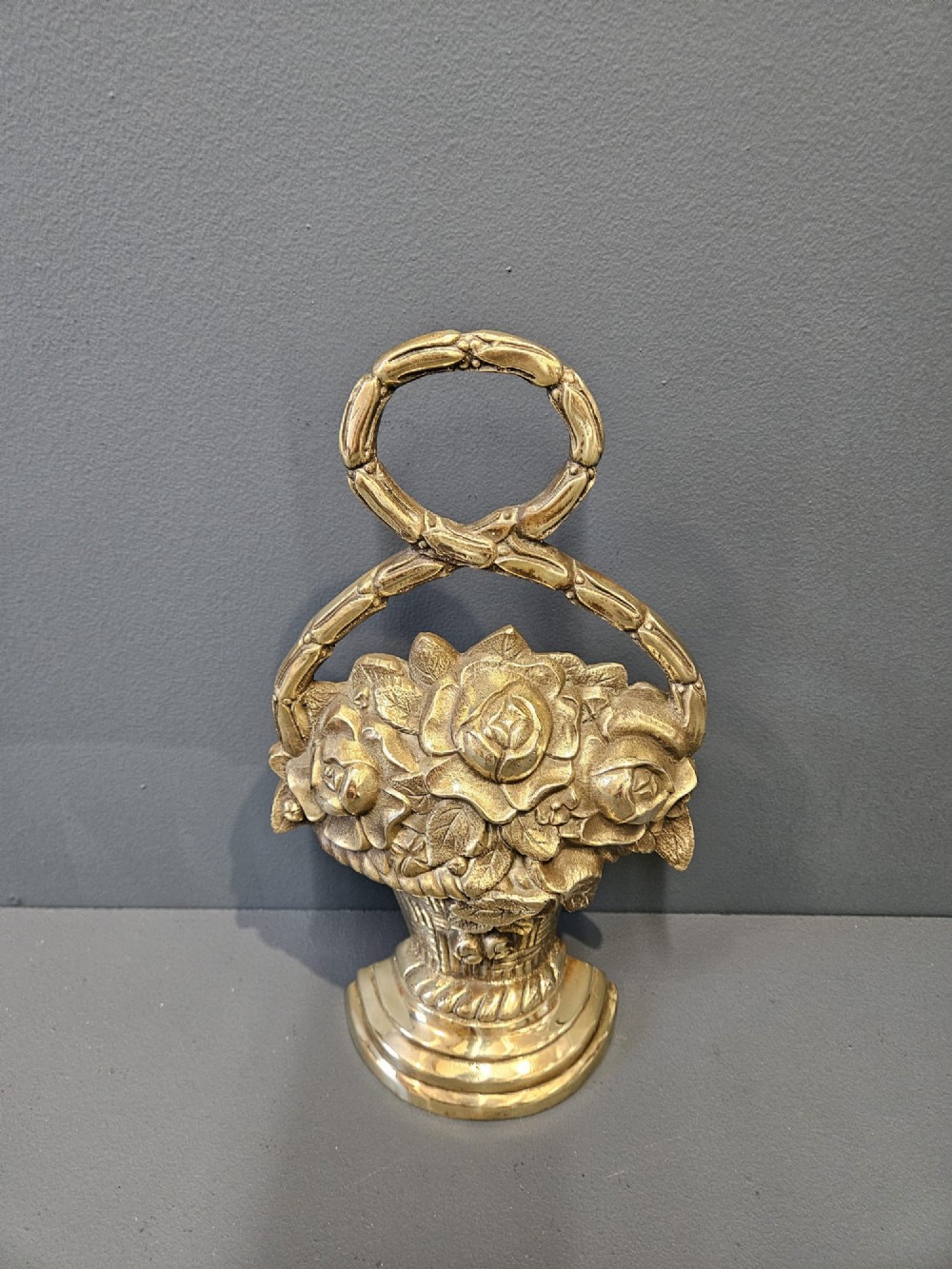 A Victorian cast brass doorstop featuring a detailed relief of roses inside a basket with an integrated loop handle. View II