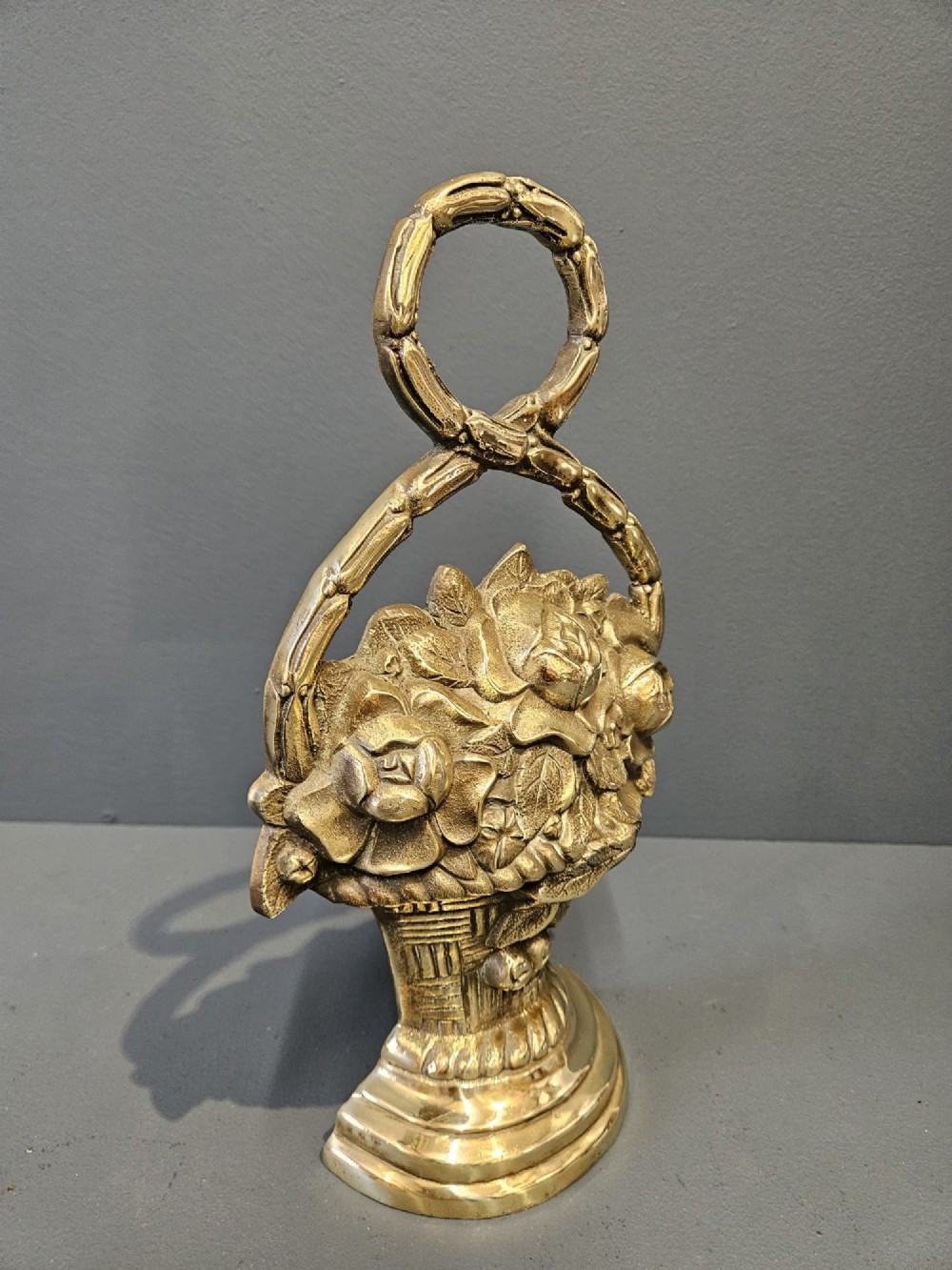 A Victorian cast brass doorstop featuring a detailed relief of roses inside a basket with an integrated loop handle. View V
