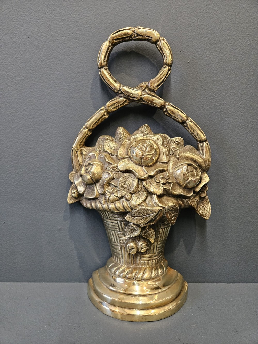 A Victorian cast brass doorstop featuring a detailed relief of roses inside a basket with an integrated loop handle. View VI