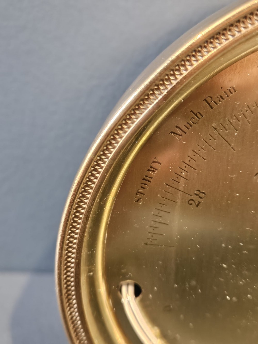 A circular Victorian brass aneroid barometer featuring an engraved face with weather markings, an integrated thermometer, and a top hanging ring. View VII
