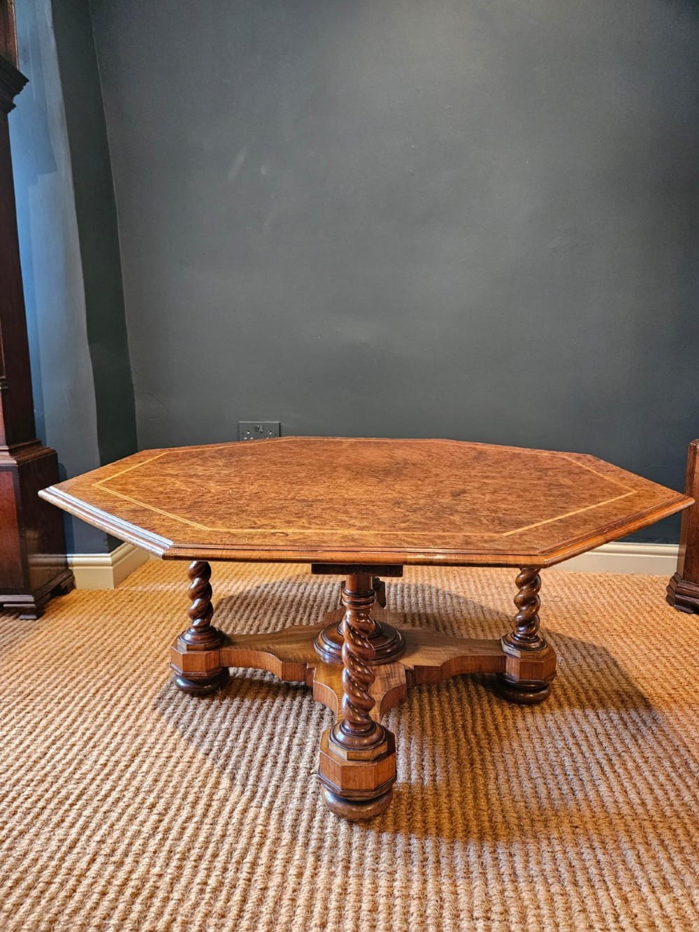 An octagonal burr walnut low coffee table featuring light wood stringing inlay, four barley twist support legs, and a central turned column on a quadruped base.