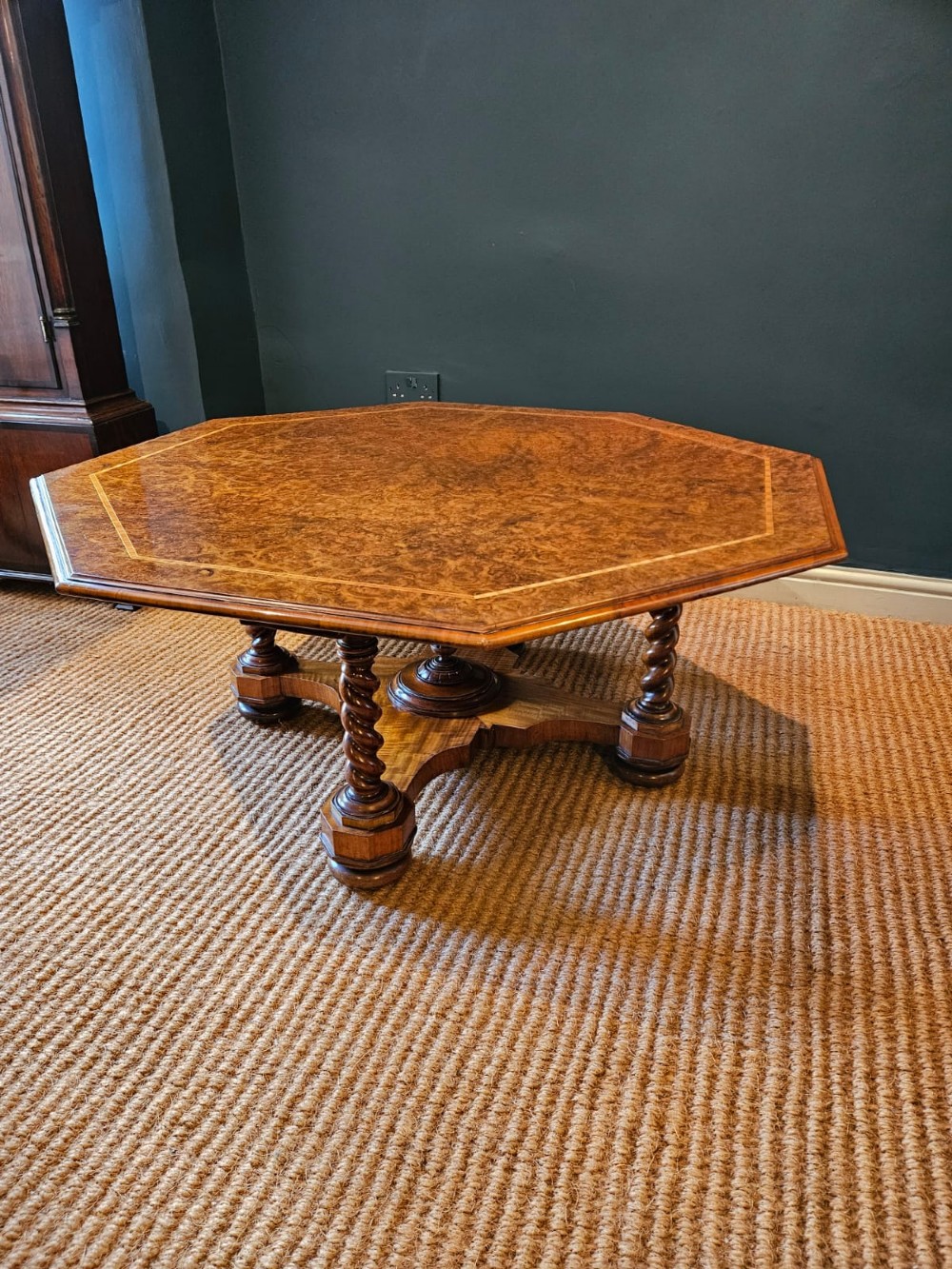 An octagonal burr walnut low coffee table featuring light wood stringing inlay, four barley twist support legs, and a central turned column on a quadruped base. View VII