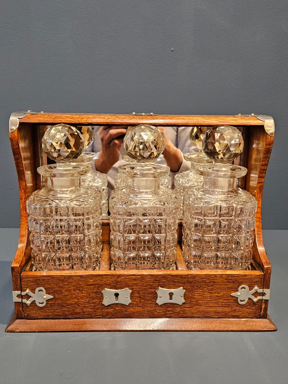 A Victorian oak three-bottle tantalus featuring silver-plated corner mounts, side handles, front keyholes, and three cut-glass decanters with multi-faceted stoppers. View III