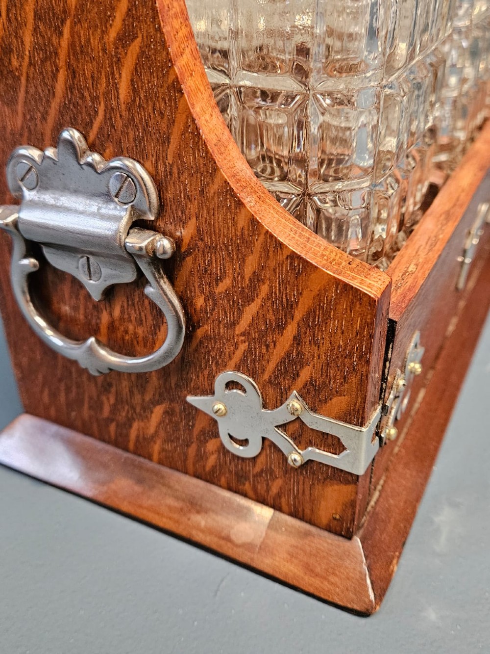 A Victorian oak three-bottle tantalus featuring silver-plated corner mounts, side handles, front keyholes, and three cut-glass decanters with multi-faceted stoppers. View IV