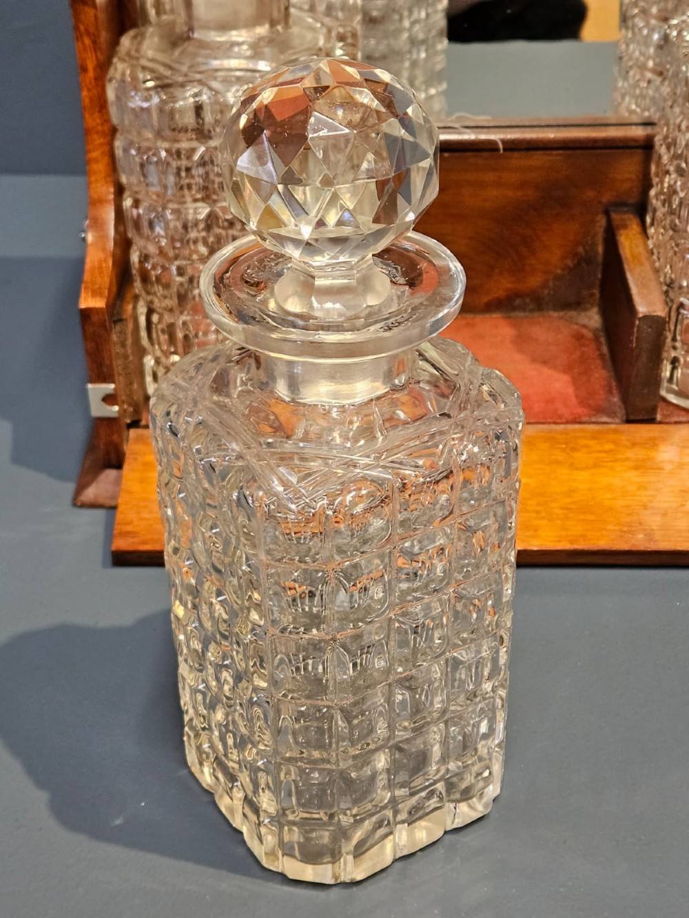 A Victorian oak three-bottle tantalus featuring silver-plated corner mounts, side handles, front keyholes, and three cut-glass decanters with multi-faceted stoppers. View VII