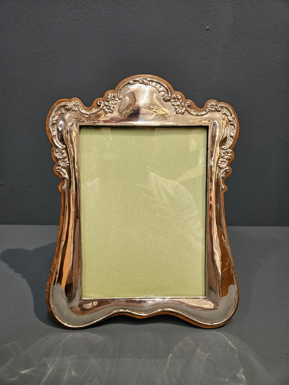 An Edwardian portrait silver photo frame featuring embossed floral detailing along a contoured edge, mounted on a solid oak back.