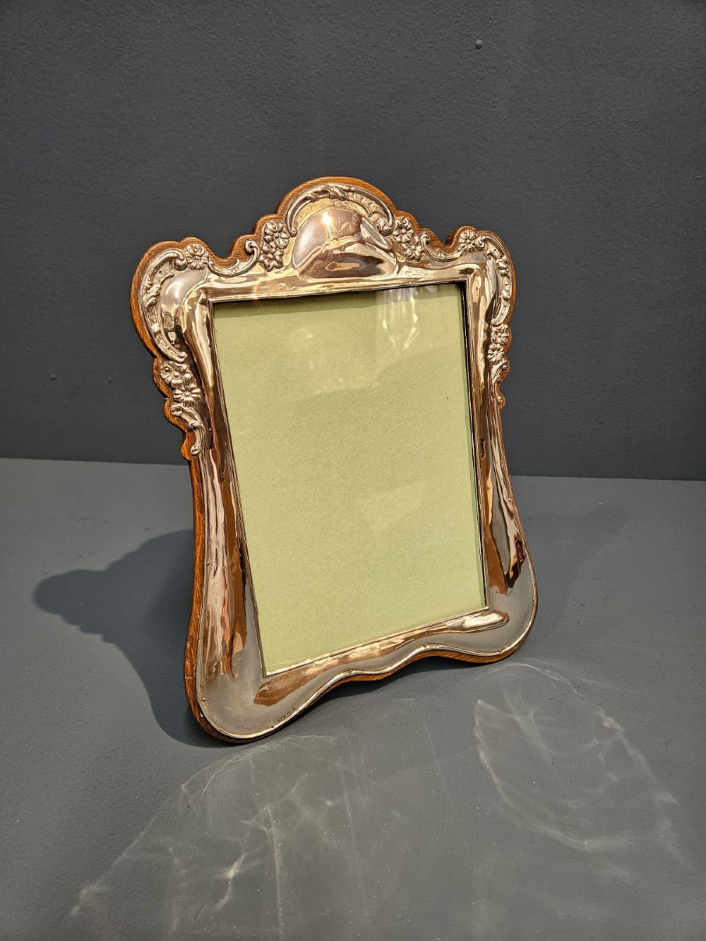 An Edwardian portrait silver photo frame featuring embossed floral detailing along a contoured edge, mounted on a solid oak back. View II