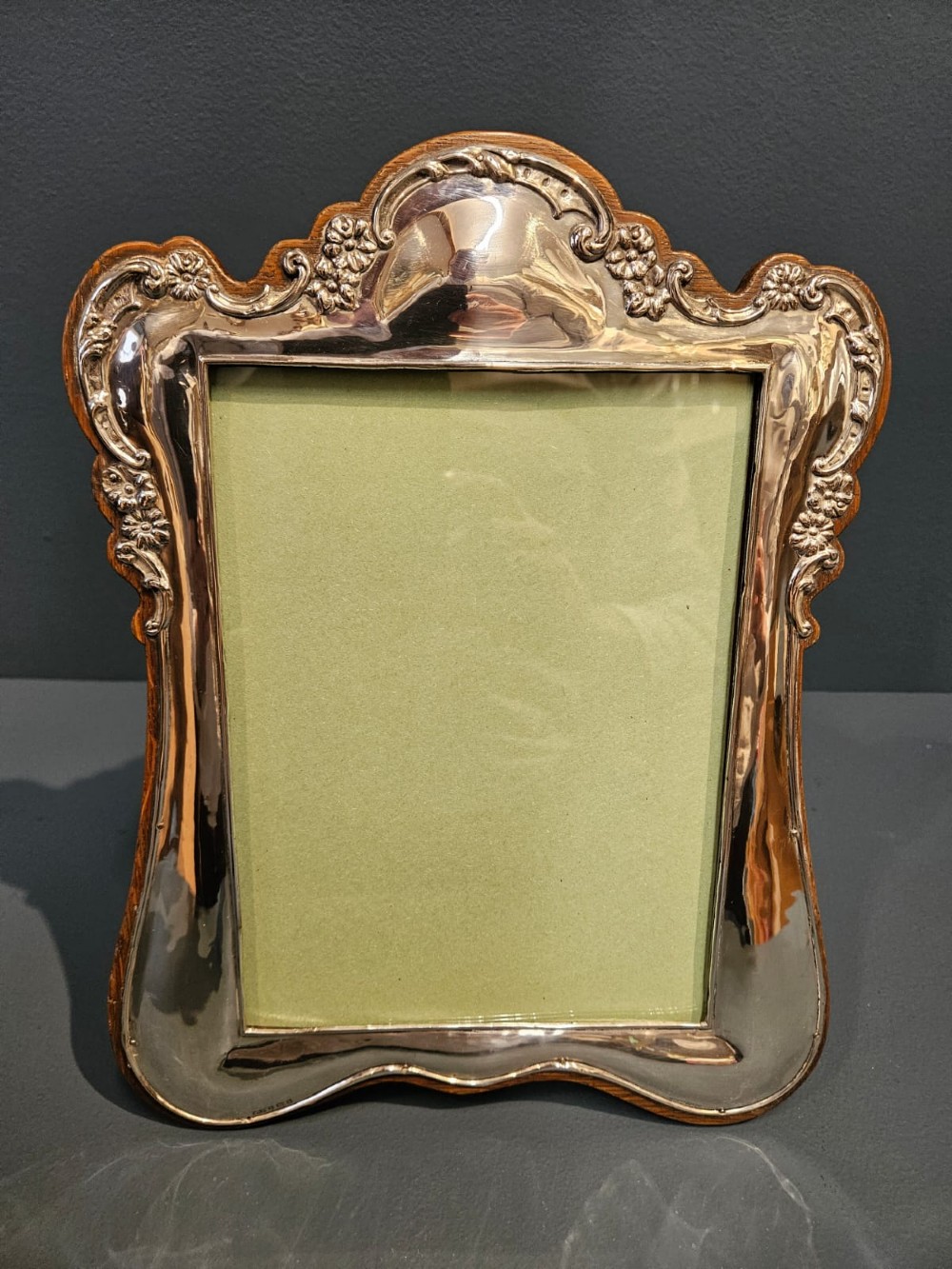 An Edwardian portrait silver photo frame featuring embossed floral detailing along a contoured edge, mounted on a solid oak back. View III