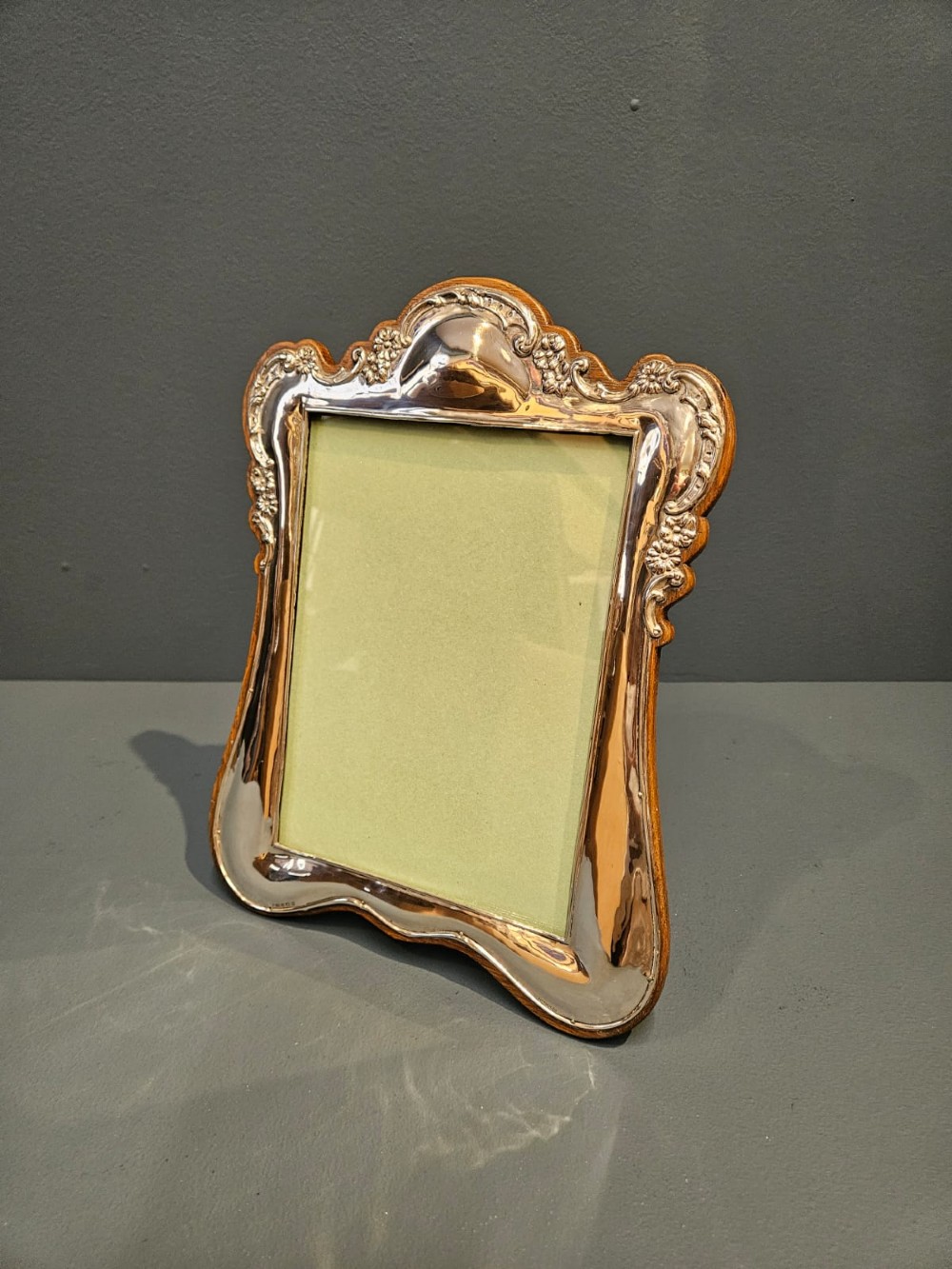An Edwardian portrait silver photo frame featuring embossed floral detailing along a contoured edge, mounted on a solid oak back. View V