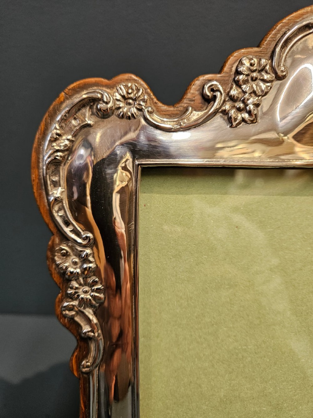 An Edwardian portrait silver photo frame featuring embossed floral detailing along a contoured edge, mounted on a solid oak back. View VI