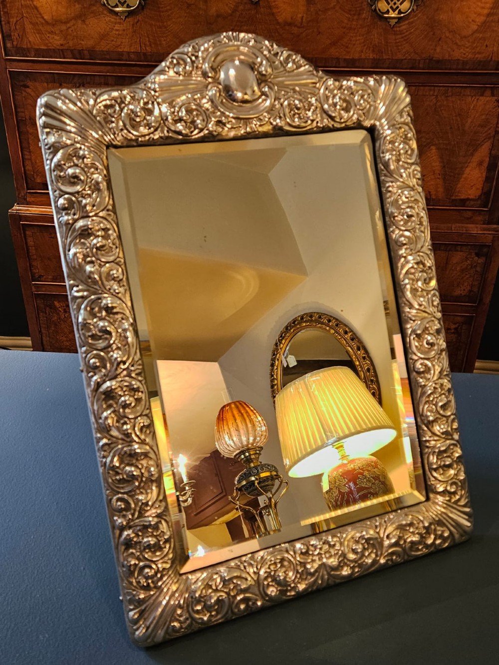 A Victorian easel-back mirror featuring an embossed silver frame decorated with scrollwork, acanthus leaves, and a central cresting cartouche around a bevelled glass plate.
