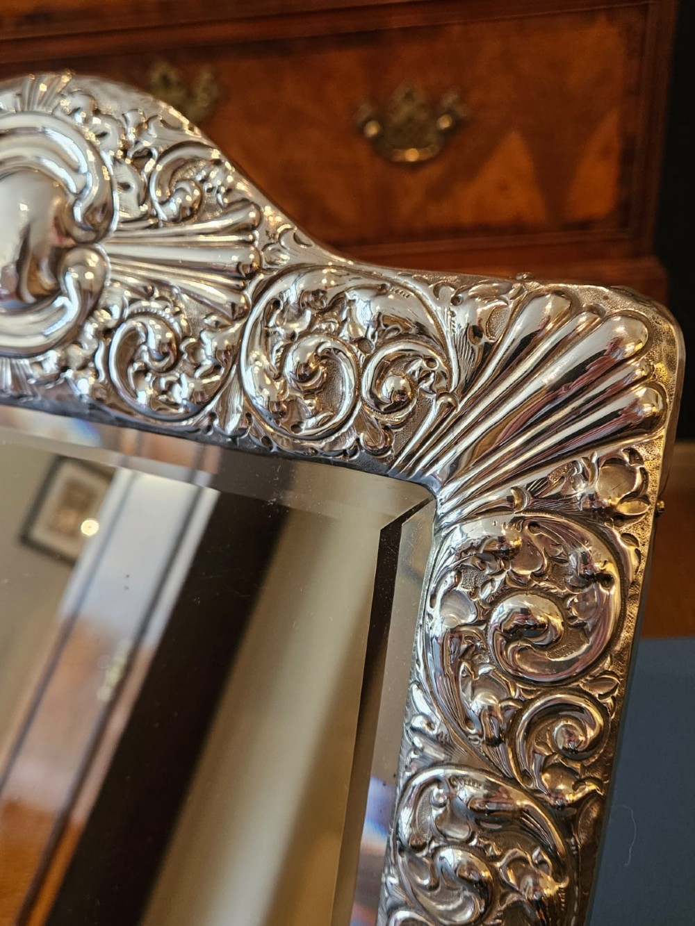 A Victorian easel-back mirror featuring an embossed silver frame decorated with scrollwork, acanthus leaves, and a central cresting cartouche around a bevelled glass plate. View II