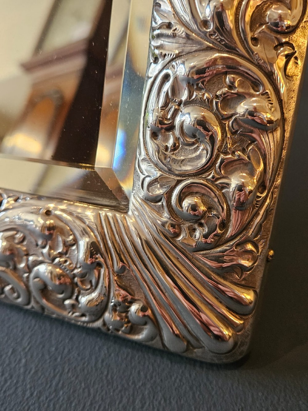 A Victorian easel-back mirror featuring an embossed silver frame decorated with scrollwork, acanthus leaves, and a central cresting cartouche around a bevelled glass plate. View IV