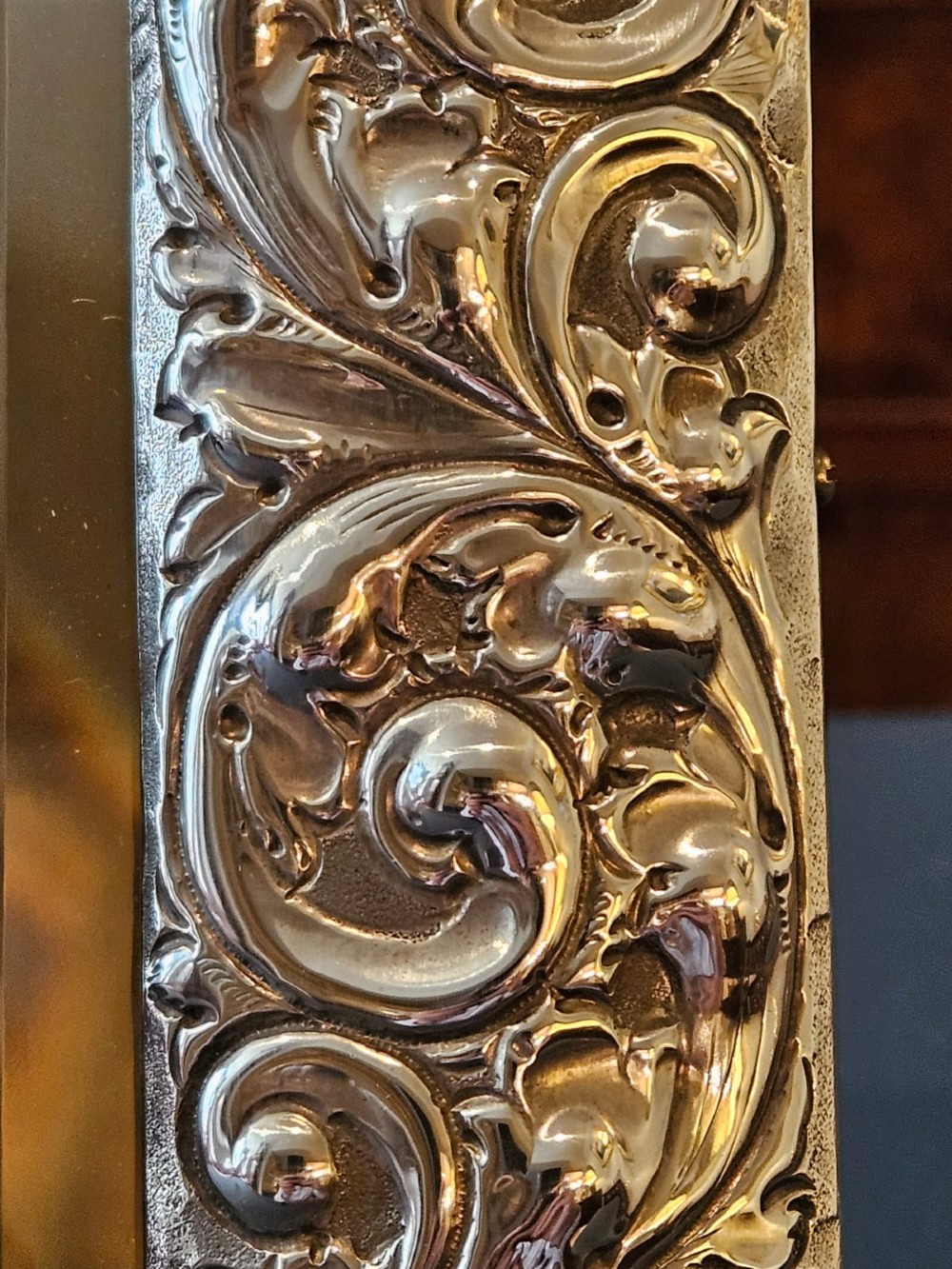 A Victorian easel-back mirror featuring an embossed silver frame decorated with scrollwork, acanthus leaves, and a central cresting cartouche around a bevelled glass plate. View VIII