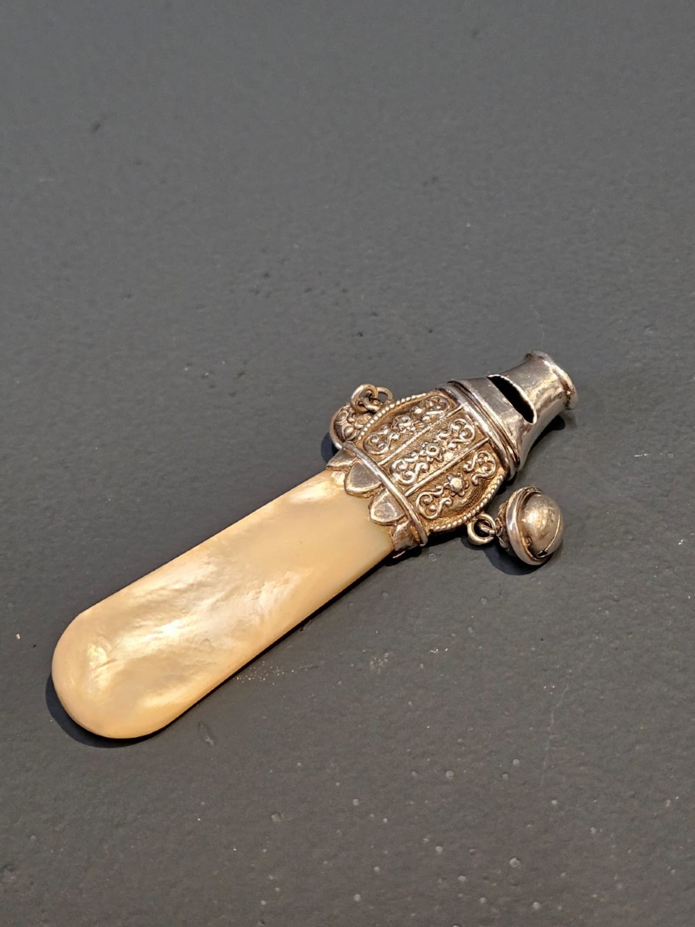 A Victorian silver and mother-of-pearl baby teether featuring a whistle end, repousse silver scrollwork, and a small hanging bell.