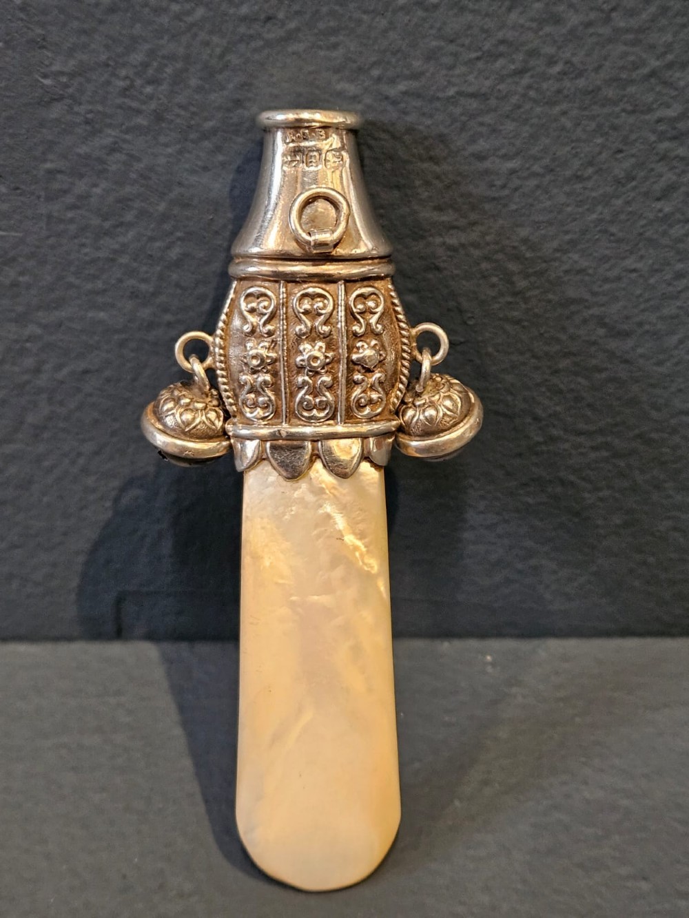 A Victorian silver and mother-of-pearl baby teether featuring a whistle end, repousse silver scrollwork, and a small hanging bell. View II