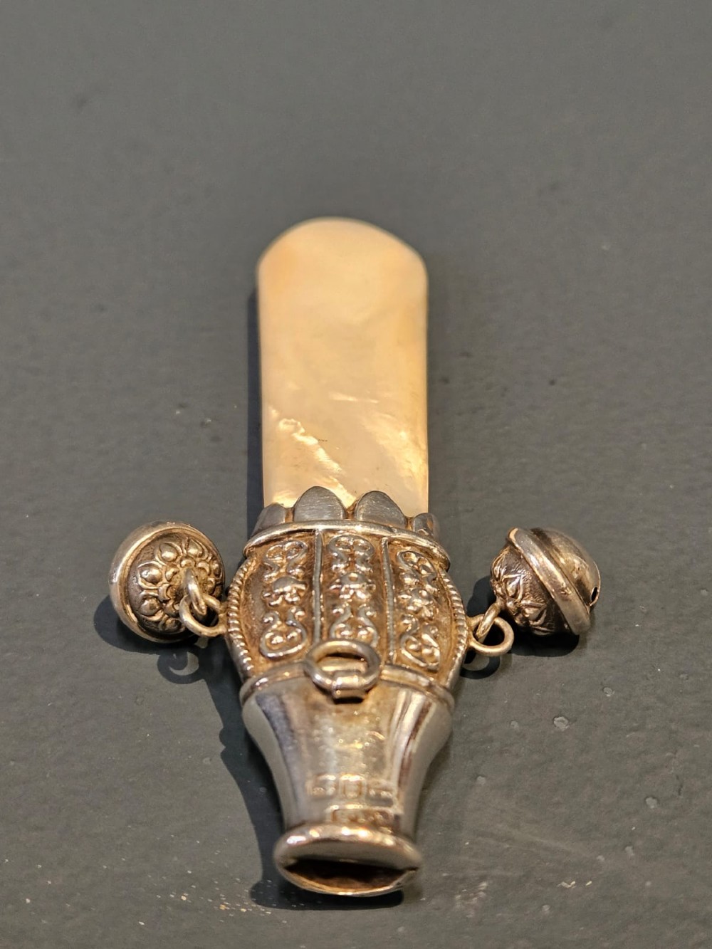 A Victorian silver and mother-of-pearl baby teether featuring a whistle end, repousse silver scrollwork, and a small hanging bell. View IV