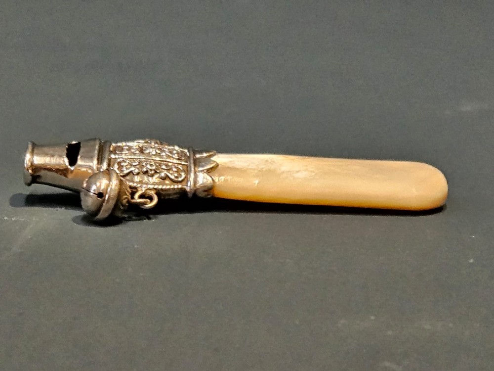 A Victorian silver and mother-of-pearl baby teether featuring a whistle end, repousse silver scrollwork, and a small hanging bell. View V