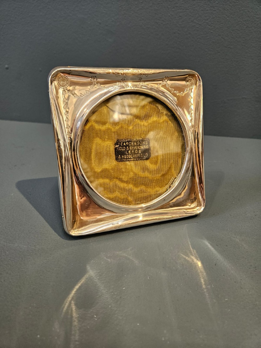 Square Edwardian silver photo frame with decorative engraved swags and a circular central window.