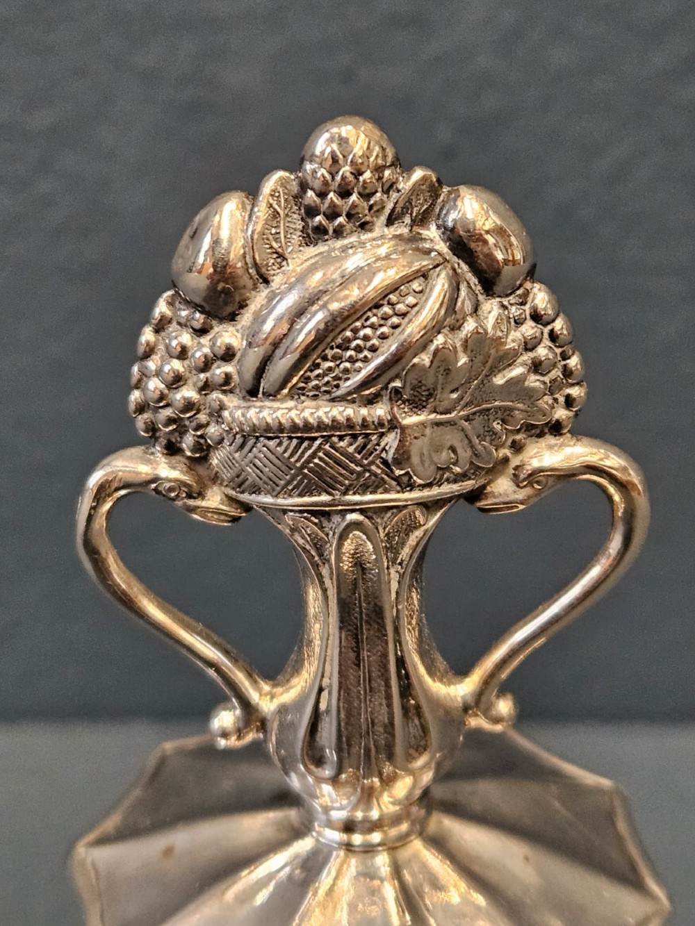 A Victorian silver table bell featuring a fruit basket finial, dual handles, a faceted body, and an embossed rim. View III